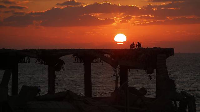 Palestinians sit atop a damaged building on a beach during sunset in the northern Gaza Strip (Photo: Reuters)