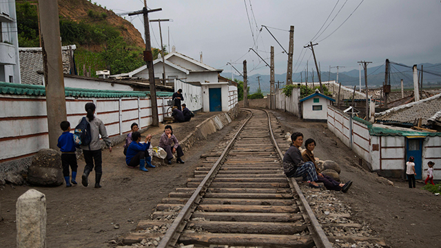 תושבים נחים לצד מסילת רכב בכפר במחוז האמגיונג (צילום: AP)