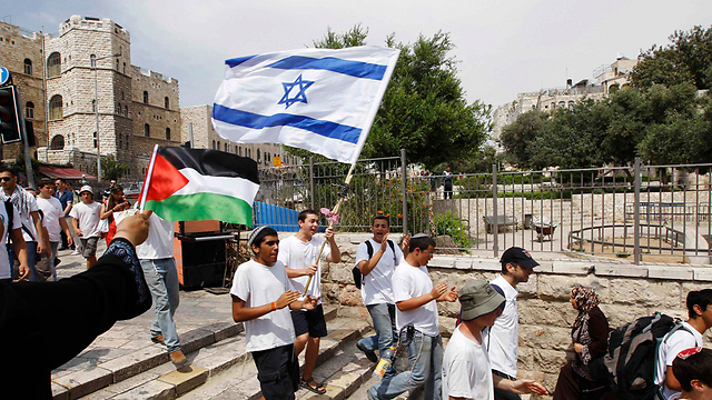 Woman waves Palestinian flag as Jewish boys march past (Photo: Reuters)