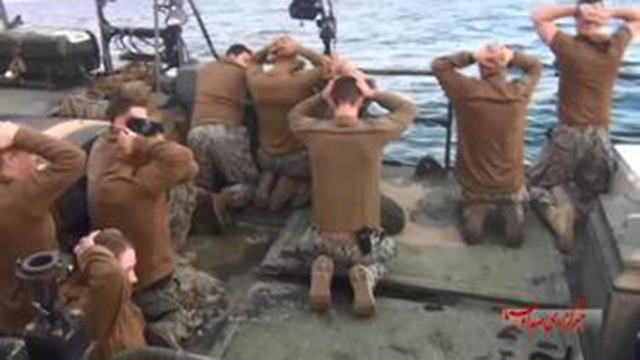 US Navy sailors kneeling with their hands on their head as Iranian forces board their boat
