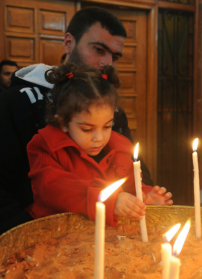 אב ובתו מדליקים נרות לכבוד החג בכנסייה בדמשק (צילום: AFP) (צילום: AFP)