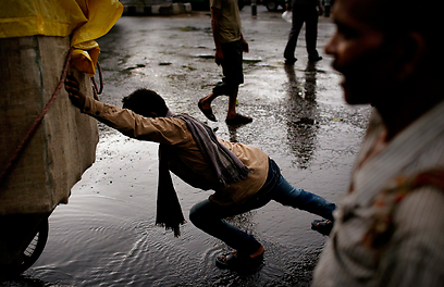 פועל הודי מנסה לפלס דרך לעגלתו בשיטפון שנוצר בניו דלהי (צילום: AP) (צילום: AP)