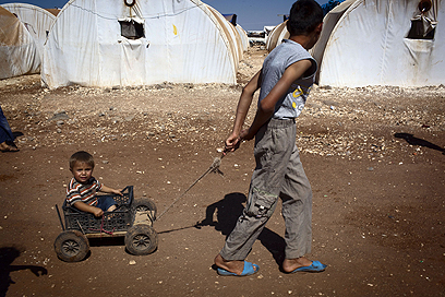 במחנה. ילד סורי מושך עגלה ובה אחיו הקטן במחנה הפליטים באב אל-סאלאם הסמוך לגבול עם טורקיה (צילום: AFP) (צילום: AFP)