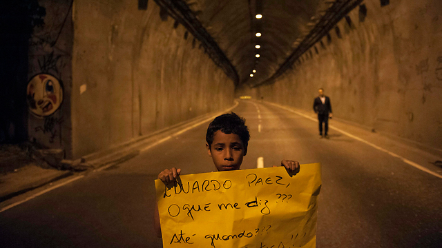 נער ברזילאי אוחז שלט שעליו נכתב "אדוארד פאאס, עד מתי?" בהתייחסו לראש העיר ריו דה ז'ניירו ולדרישה לחקור מה עלה בגורל עשרות אלפי האנשים שנעלמו באופן מסתורי באזור (צילום: AP) (צילום: AP)