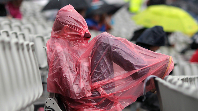 אוהד קריקט מגן על עצמו מפני הגשם ביציע הקהל של טורניר הקריקט השנתי במנצ'סטר. הסופה גרמה להפסקה בלתי מתוכננת במהלך משחק בין אנגליה ואוסטרליה ביום החמישי של הטורניר (צילום: AFP) (צילום: AFP)