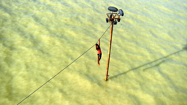 צעיר הודי נאחז בכבל חשמל מעל לשטפון בנהר הגנגס. עונת המונסונים באזור צפויה להסתיים בחודש ספטמבר (צילום: AFP) (צילום: AFP)