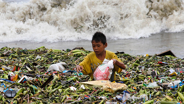 ילד חופר בהררי זבל בפיליפינים, כשברקע רוחות הטייפון "אוטור" (צילום: רויטרס) (צילום: רויטרס)