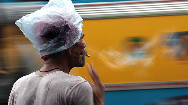 נהג ריקשות בכלכותה, הודו, מוצא מגן ניילון מפני הגשם השוטף (צילום: EPA) (צילום: EPA)