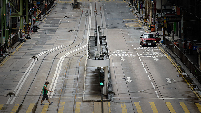 אדם חוצה כביש שומם בהונג קונג, האזור המנהלי המיוחד של סין. רובע העסקים של הונג קונג נסגר השבוע ונותר שומם בעקבות אזהרה מפני סופת טייפון קרבה (צילום: AFP) (צילום: AFP)
