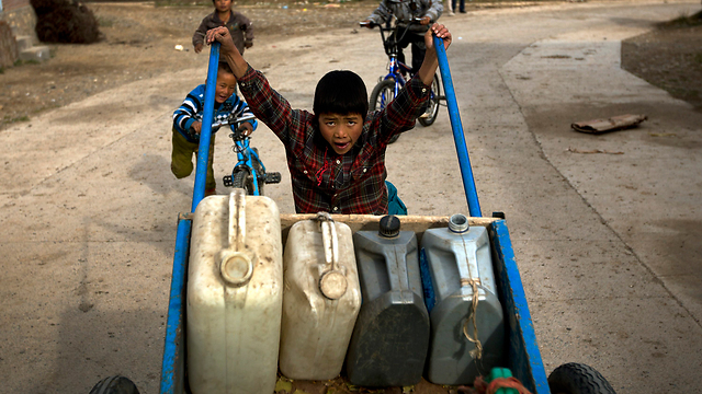 ילד טיבטי דוחף עגלה עם מכלי מים בדרכו לבאר בכפר בג'יאו בסין. על פי ההערכות, הכפר קיים כ-2,000 שנה (צילום: AP) (צילום: AP)