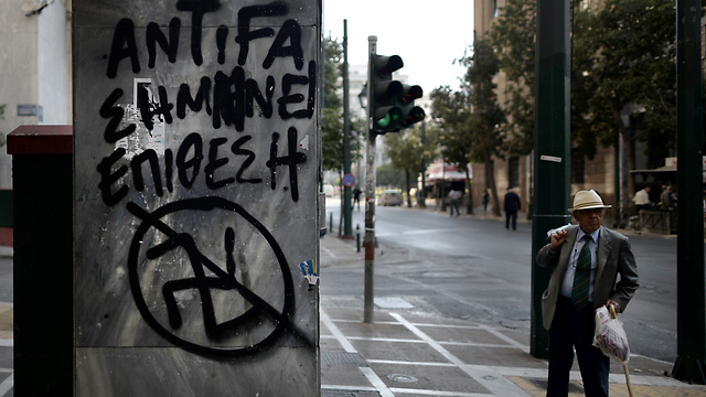 אדם מבוגר עובר ברחוב באתונה ליד כתובת גרפיטי נגד פאשיזם ביוון: "אנטי-פאשיזם משמעותו התקפה" (צילום: AFP) (צילום: AFP)