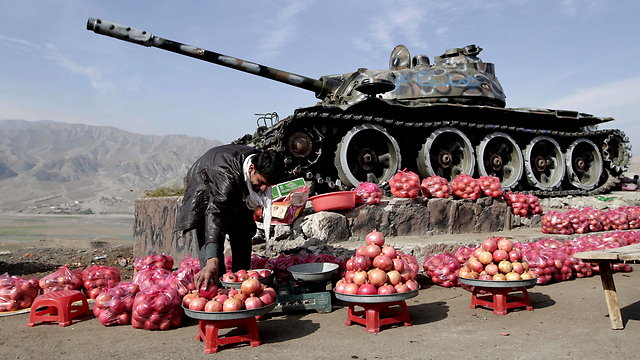 רוכל אפגני מציב את סחורתו לצד טנק סובייטי ישן בעיר סורובי שבמחוז קאבול (צילום: AP) (צילום: AP)
