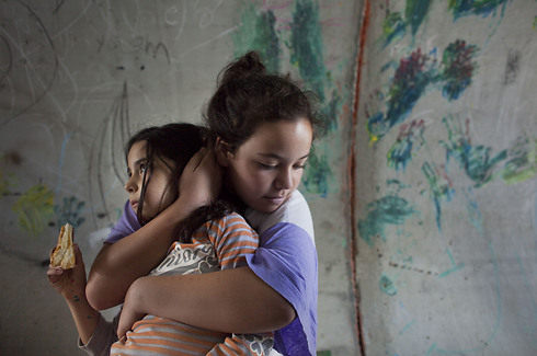 ילדה מחבקת את אחותה בעת אזעקה, ומכסה את אוזניה כדי לעמעם את קולו של צופר האזעקה, במקלט מאולתר ביישוב ניצן (צילום: אוריאל סיני / גטי אימג'ס) (צילום: אוריאל סיני / גטי אימג'ס)