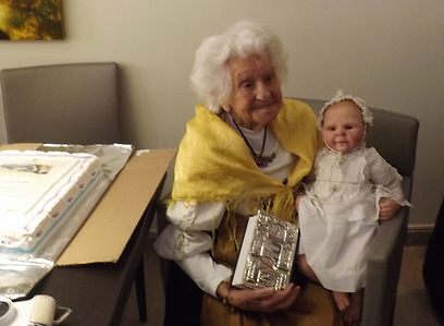 Oma Ella at her 104th birthday celebrations, holding a silver-bound Bible, a gift from the Tourism Ministry, and a handmade doll in her likeness, wearing the clothes in which she was christened (Photo courtesy of the Tourism Ministry)