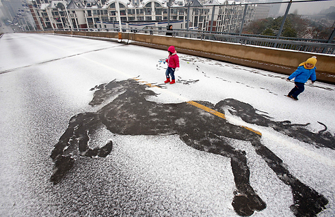 ילדים משחקים בשלג ליד דמות של סוס שנוצרה מטביעות רגל בעיר ווהאן בסין (צילום: AP) (צילום: AP)