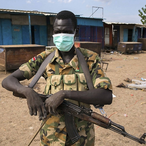 חייל דרום סודן עומד ליד המסגד שבו בוצע הטבח ולצדו מוטלת גופה (צילום: רויטרס) ()