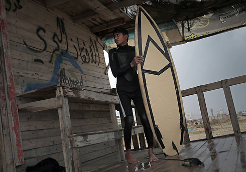 Palestinian Ahmed Abu Ghanim, 16, holds his surf board while standing next to Arabic writing that reads 'lifeguard' (Photo: AP) (Photo: AP)