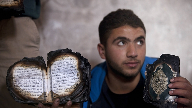 Resident of Mughayer holds up Koran and other artifact burned as a result of the mosque fire. (Photo: Associated Press) (Photo: Associated Press)