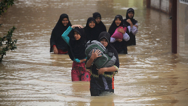 נשים תאיות חוצות דרך מוצפת מים לאחר שגשמים כבדים ירדו בעיר הדרומית נראטיוואט. בשבוע האחרון הוצפו חלקים רבים בדרום תאילנד בעקבות מזג האוויר הסוער (צילום: AFP) (צילום: AFP)