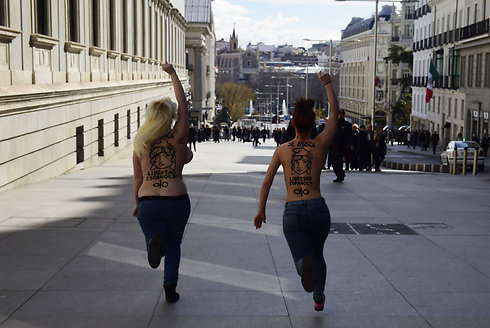 פעילות בארגון הפמיניסטי "פמן"  רצות חשופות חזה עם המסר "אנחנו מחפשות חירות ספרדית" במהלך הפגנה למען הזכות להפגין מחוץ לבניין הפרלמנט במדריד (צילום: AFP) (צילום: AFP)