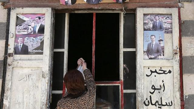 Syrian woman grabs bag of bread in Damascus at shop decorated with pictures of PresidenT al-Assad (Photo: AP) (Photo: AFP)