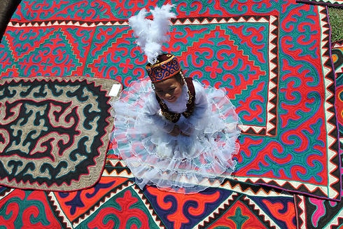 ילדה לבושה בבגדים קירגיזיים מסורתיים יושבת על שטיח בפסטיבל הבינלאומי החמישי של אמנות שימושית קירגיזית. אמנים מכל רחבי קירגיזסטן השתתפו בפסטיבל שזכה לתמיכה גרמנית (צילום: AFP) (צילום: AFP)