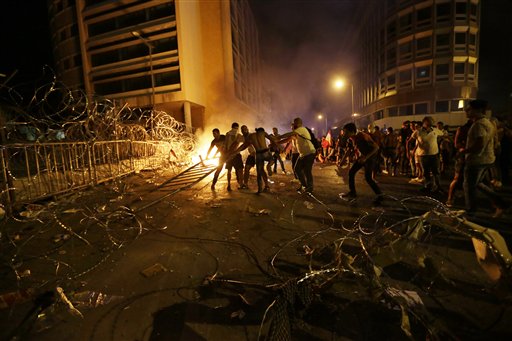  Lebanese protesters set fire to barriers and trash behind the barbed wire separating them from the police (Photo: AP)