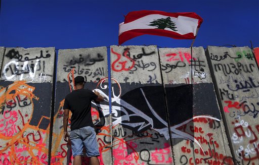 A Lebanese activist paints graffiti on a concrete wall, installed by authorities, near the main Lebanese government building (Photo: AP)
