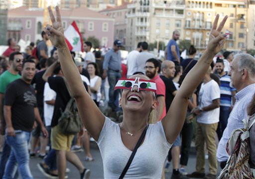 A Lebanese anti-government protester flashes victory signs as she wears glasses made from Lebanese flags (Photo: AP)