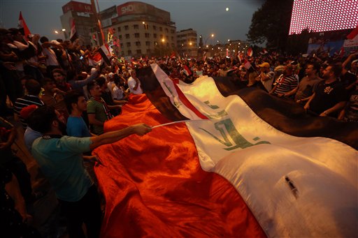 Protesters chant slogans in support of Iraqi Prime Minister Haider al-Abadi as they carry a large national flag during a rally in Tahrir Square in Baghdad (Photo: AP)