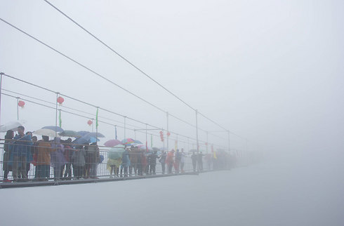 תיירים בסין הולכים בזהירות על גשר זכוכית בהרי שינויזאי. הגשר, שבמקור נבנה מעץ, נפתח מחדש לפני שנתיים במטרה להיות אטרקציה תיירותית (צילום: AFP) (צילום: AFP)