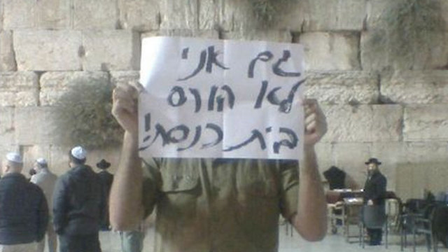 An IDF soldier holds a sign saying "I too won't demolish a synagogue," in front of the Western Wall. (Photo: Facebook)
