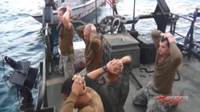 US Navy sailors kneeling with their hands on their head as Iranian forces board their boat