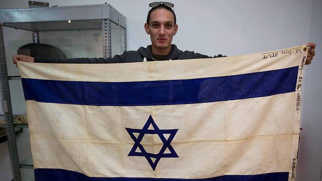 An employee of the Kedem Auction House in Jerusalem showing the flag of the iconic ship the SS Exodus, the most famous of hundreds of ships that sought to transport European Jews to the land that later became the nation of Israel immediately after World War II. (Photo: AFP)