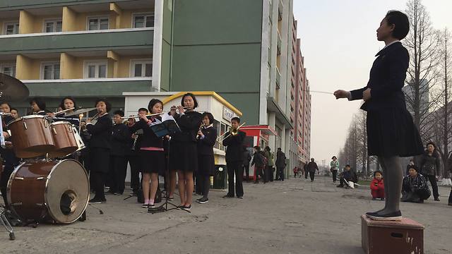 תלמידי בית ספר מנגנים לעוברים ושבים ברחוב בפיונגיאנג, בירת צפון קוריאה, כדי להנעים את זמנם בדרך מהעבודה הביתה (צילום: AP) (צילום: AP)