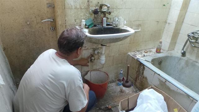 דייב, מתנדב העמותה מתקן סתימה בכיור בביתו של ניצול שואה (צילום: העמותה לעזרה מיידית לניצולי שואה) (צילום: העמותה לעזרה מיידית לניצולי שואה)