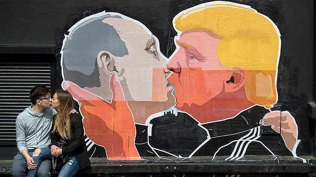 זוג מתנשק בווילנה, בירת ליטא, על רקע כרזה גדולה ועליה תמונות טראמפ ופוטין מתנשקים (צילום: AP) (צילום: AP)