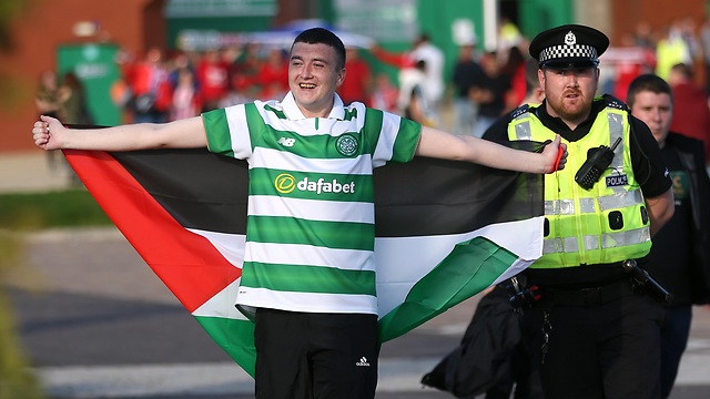 A Celtic fan with a Palestinian flag is escorted by a Police officer away from Hapoel Beer-Sheva fans outside the stadium before the match (Photo: Reuters) (Photo: Reuters)