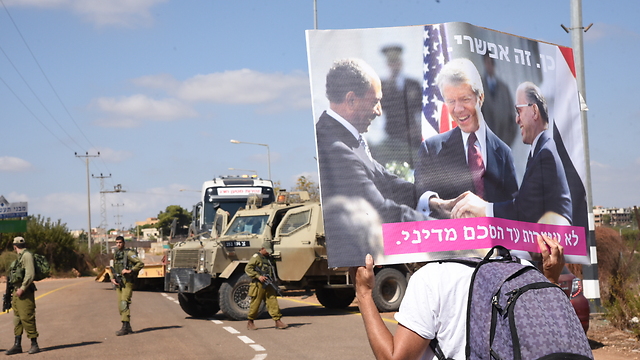 A protester carrying a sign with Mencahem Begin, Anwar Sadat and Jimmy Carter sign the Israel-Egypt Peace Treaty (Photo: Avihu Shapira)