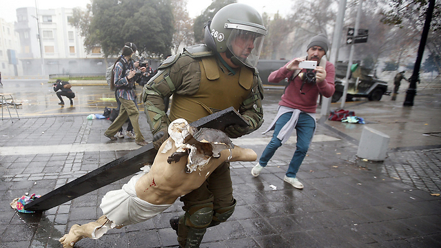 Policeman recovers a crucifix taken from the National Gratitude Church during a student protest in Chile. (Photo: EPA)
