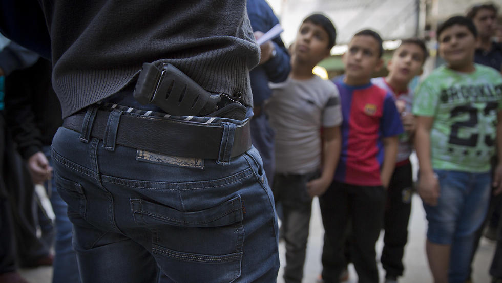 Palestinian refugee boys gather by armed men who are wanted by the Palestinian Authority security, one with a concealed weapon (Photo: AP)