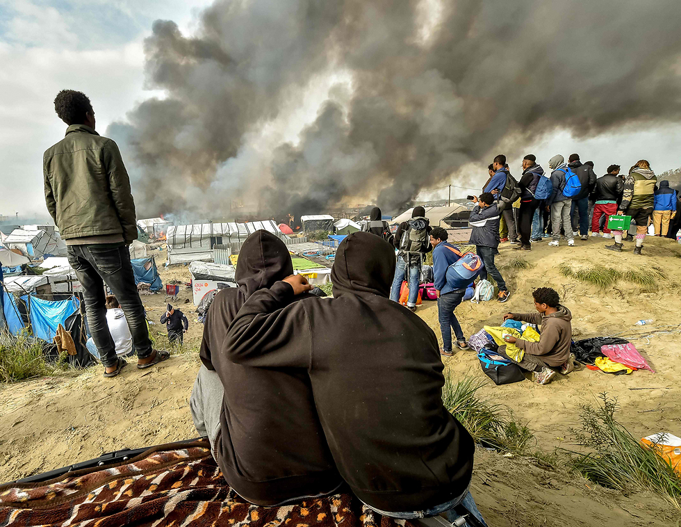 מהגרים שהשתכנו במחנה הפליטים הפיראטי "הג'ונגל" בצרפת צופים באש עולה מהמחנה בעת פירוקו באוקטובר (צילום: AFP) (צילום: AFP)