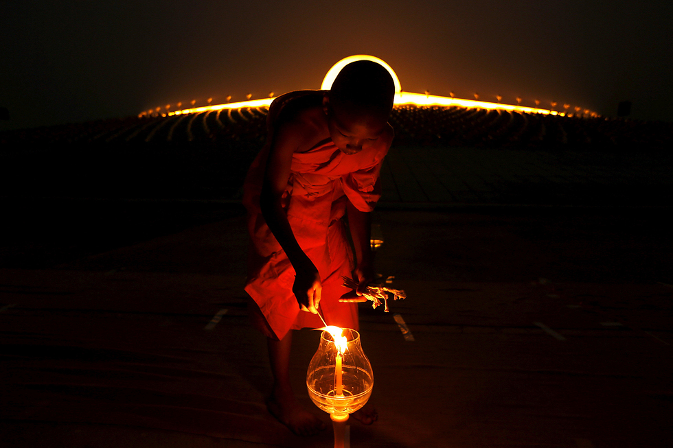 נזיר בודהיסטי מדליק נר מצפון לבגקוק, תאילנד (צילום: רויטרס) (צילום: רויטרס)