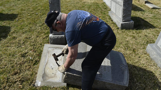 A volunteer helps to restore and repair vandalized headstones (Photo: EPA)