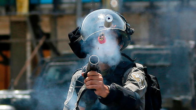 Israeli policeman fires tear gas at Palestinian rioters near Beit El (Photo: AFP)