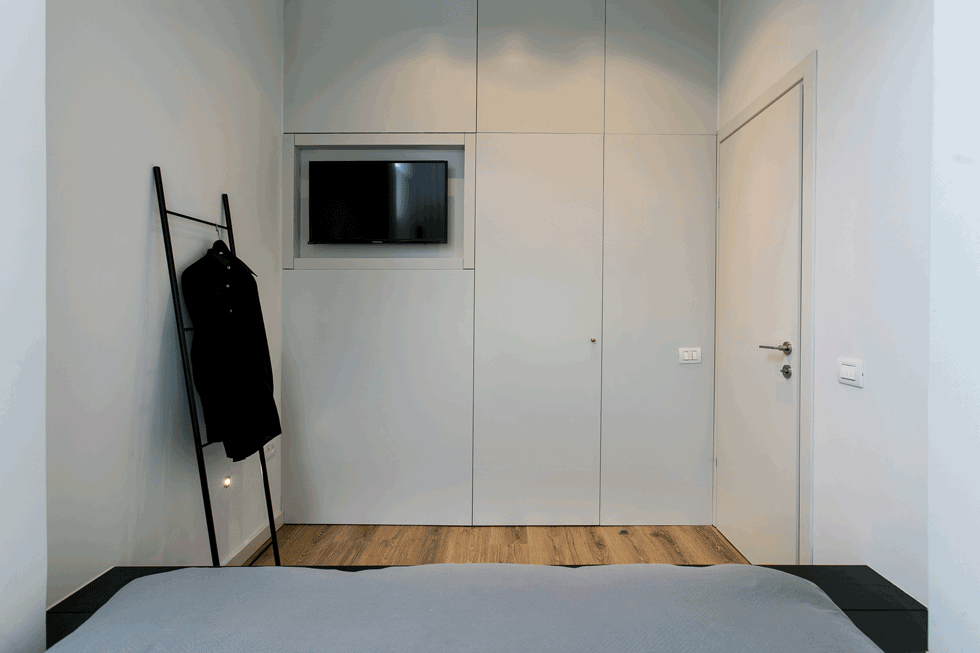 חדרו של האב: המזרון מונח על במת עץ שחורה. דלת שמוטמעת בארון הקיר הלבן נפתחת אל חדר ארונות ואזור שירות עם מכונות כביסה וייבוש (צילום: שירן כרמל)