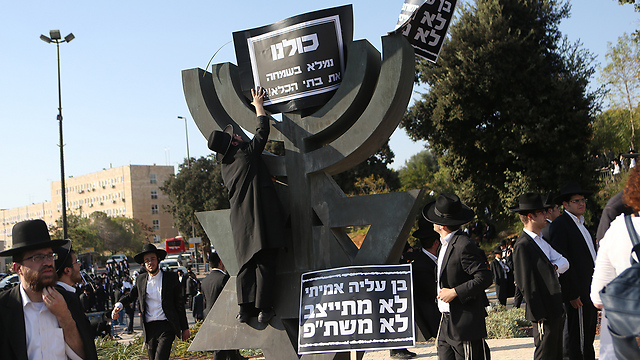 Haredi protesters near the Knesset, hanging a sign saying, "We'll happily fill the prisons" (Photo: Alex Kolomoisky)