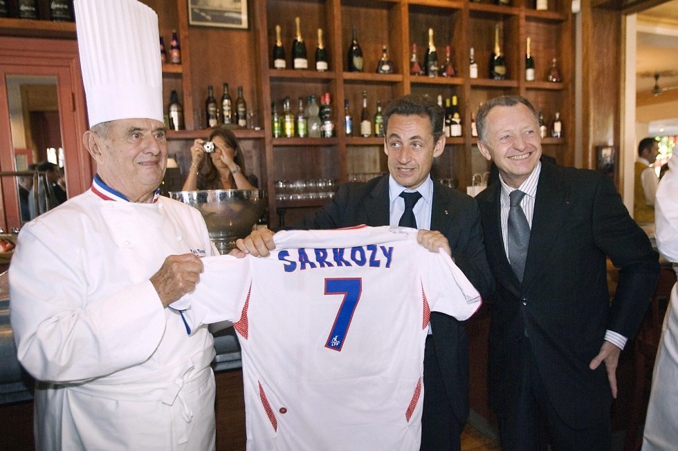 נשיא צרפת ניקולה סרקוזי מחזיק בחולצת כדורגל עם שמו עליה, יחד עם שף פול בוקוז במסעדתו ארגנזו בעיר ליון, במהלך 2007 (  ) (  )