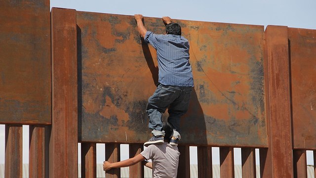 מהגר מ מקסיקו סיודאד חוארס מטפס מעל גדר מתכת חומה ועובר ל ארה