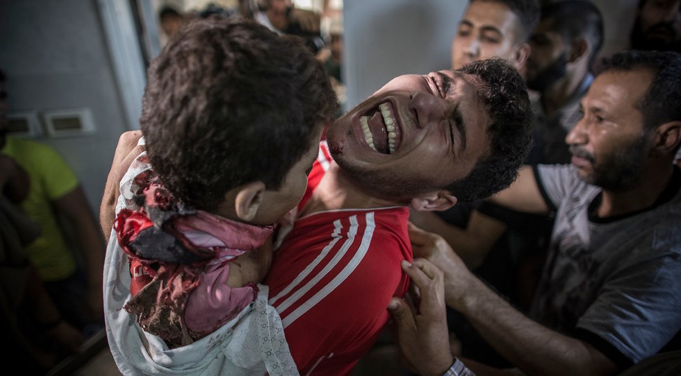 Palestinian man cries as he holds the dead body of his young brother shortly after he got killed by an Israeli naval bombardment in the port of Gaza City (Photo: EPA)